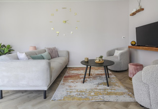 Moderne stue på Eco Lodge ved Uniq Leisure i Holland med lyse møbler, vægur og fladskærms-tv.