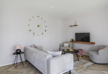 Sala de estar moderna con muebles grises, reloj de pared y TV en Eco Lodge de Uniq Leisure, Países Bajos.