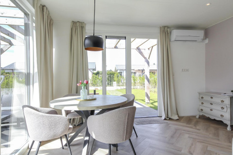 Lyst og moderne spiseområde i Eco Lodge på Uniq Leisure, med runde borde, komfortable stole og udsigt til haven.