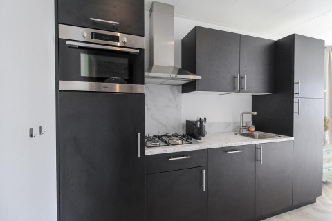 Cocina negra moderna en Eco Lodge de Uniq Leisure en los Países Bajos con horno, estufa de gas y encimera de mármol.