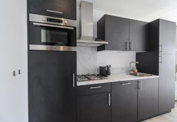Modern black kitchen at Eco Lodge at Uniq Leisure in the Netherlands with oven, gas stove, and marble countertop.