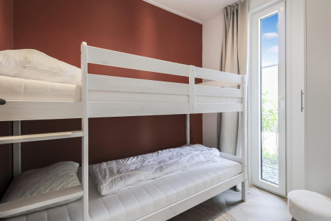 Habitación luminosa con literas blancas y acceso al jardín por puerta de cristal en Eco Lodge en Uniq Leisure, Países Bajos.