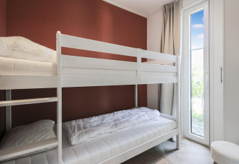 Habitación luminosa con literas blancas y acceso al jardín por puerta de cristal en Eco Lodge en Uniq Leisure, Países Bajos.