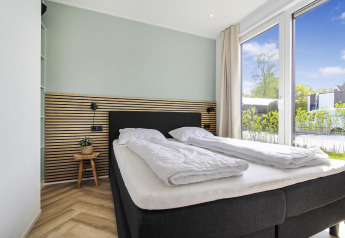 Modern, bright bedroom at Eco Lodge at Uniq Leisure in the Netherlands, featuring large windows and sunlight.
