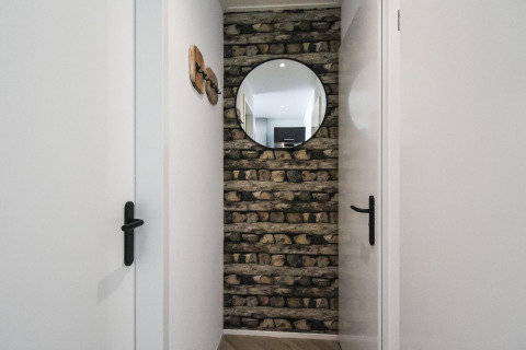 Pasillo estrecho con pared de piedra, espejo redondo y puertas blancas en Eco Lodge en Uniq Leisure, Países Bajos.