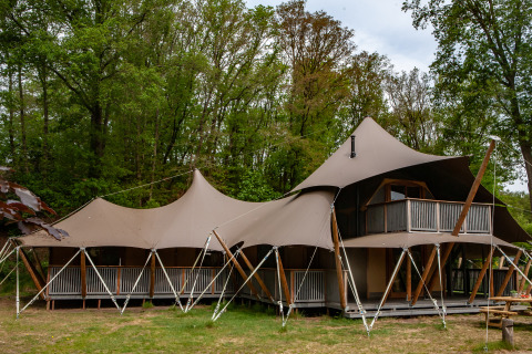 Safari-Zelt Kings Lodge mit Whirlpool im Sandberghe, Niederlande, von außen im Waldumfeld gesehen.