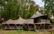 Safari-Zelt Kings Lodge mit Whirlpool im Sandberghe, Niederlande, von außen im Waldumfeld gesehen.