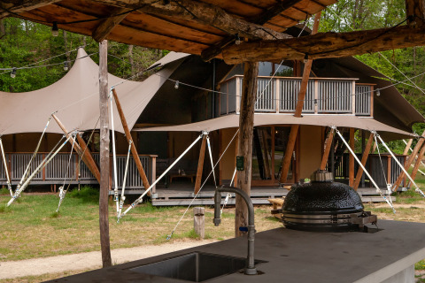 View of Kings Lodge safari tent with balcony and outdoor kitchen featuring grill at Sandberghe in the Netherlands.
