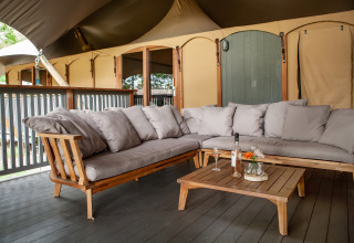 Gemütlicher Outdoor-Loungebereich mit grauem Sofa beim Safarizelt Kings Lodge + Hot Tub in Sandberghe.