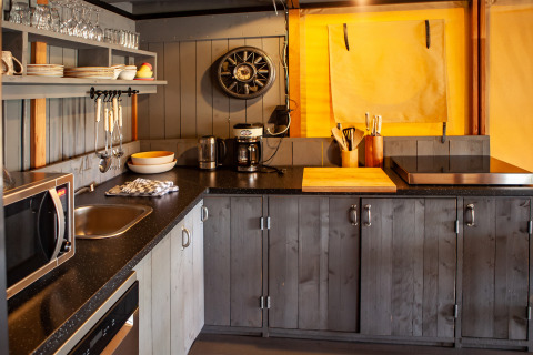 Modern safari tent kitchen at Kings Lodge + Hot Tub in Sandberghe, Netherlands, with wooden cabinets.