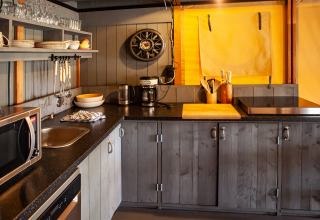 Modern safari tent kitchen at Kings Lodge + Hot Tub in Sandberghe, Netherlands, with wooden cabinets.