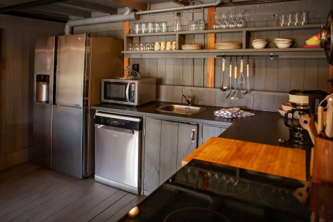Cocina moderna con gabinetes grises, estantes abiertos, refrigerador, microondas y utensilios en tienda.