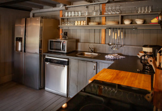 Modern kitchen area with grey cabinets, open shelves, fridge, microwave, and utensils inside a tent.