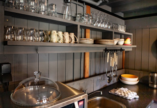 Acogedora zona de cocina con estantes abiertos, vasos y platos en Kings Lodge en Sandberghe, Países Bajos.