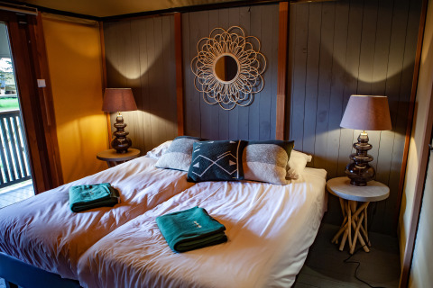 Dormitorio acogedor en la tienda safari Kings Lodge en Sandberghe, Países Bajos, con cama doble y lámparas.