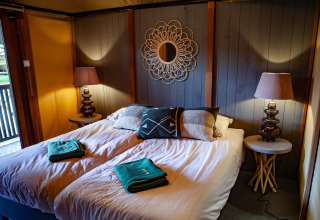 Dormitorio acogedor en la tienda safari Kings Lodge en Sandberghe, Países Bajos, con cama doble y lámparas.