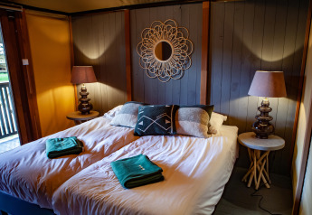 Dormitorio acogedor en la tienda safari Kings Lodge en Sandberghe, Países Bajos, con cama doble y lámparas.
