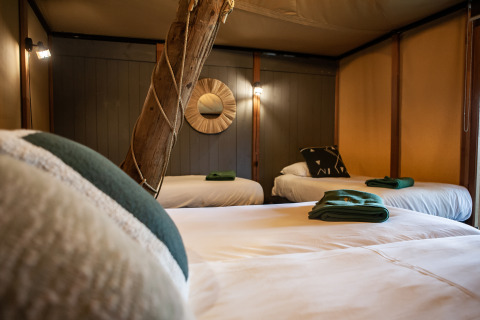 Interior de la tienda safari Kings Lodge en Sandberghe, Países Bajos, con tres camas y detalles rústicos.