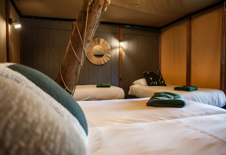 Interior de la tienda safari Kings Lodge en Sandberghe, Países Bajos, con tres camas y detalles rústicos.