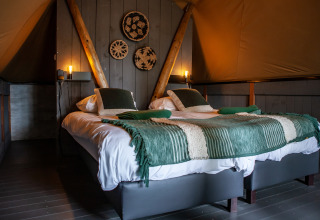 Vista interior de tienda safari Kings Lodge con dos camas, mantas verdes y decoración de pared en Sandberghe.
