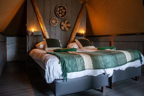 Interieur van de Kings Lodge safaritent met twee bedden, groene plaids en wanddecoratie bij Sandberghe.