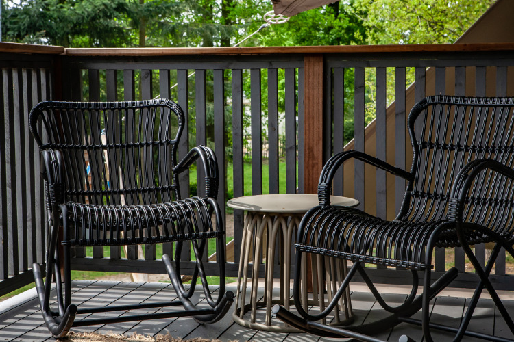 Two black rocking chairs and a small table on a terrace overlooking greenery at Sandberghe in the Netherlands.
