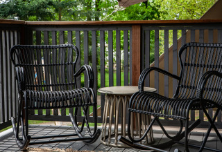 Two black rocking chairs and a small table on a terrace overlooking greenery at Sandberghe in the Netherlands.