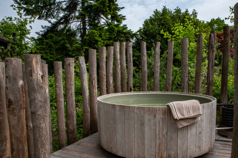 Outdoor hot tub with towel, surrounded by wooden posts and greenery at Kings Lodge, Sandberghe, Netherlands.
