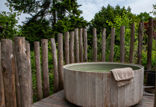 Outdoor-Holz-Whirlpool mit Handtuch, umgeben von Holzpfosten und Natur bei Kings Lodge, Sandberghe, Niederlande.