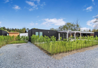 Eco Lodge moderna con fachada negra, camino de grava, plantas verdes y cielo azul en un día soleado.