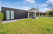 Eco Lodge moderna con fachada negra, grandes ventanales y terraza rodeada de césped verde y cielo azul.