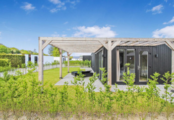 Eco Lodge moderna de fachada negra con pérgola de madera y jardín verde bajo un cielo azul claro.