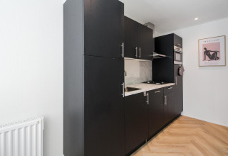 Pequeña cocina negra moderna en Eco Lodge, suelo de madera, armarios oscuros y obra de arte en la pared.