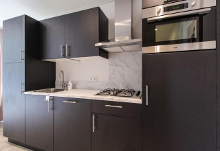 Cocina moderna en Eco Lodge con gabinetes oscuros, horno empotrado, encimera de mármol y estufa de gas.