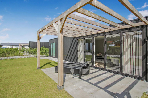 Terraza exterior con pérgola de madera en Eco Lodge, modernas paredes negras y grandes ventanales al jardín.