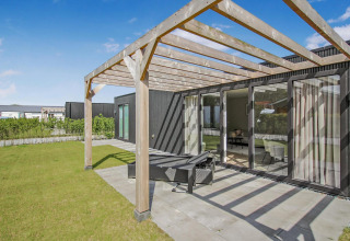 Udendørs terrasse med træpergola ved Eco Lodge, moderne sorte vægge og store glasdøre mod haven.