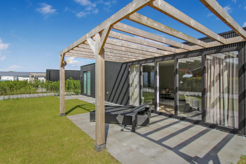 Patio soleado con pérgola de madera en Eco Lodge, puertas de cristal modernas y césped verde cuidado.