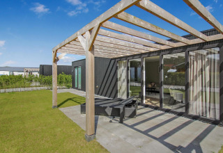Patio soleado con pérgola de madera en Eco Lodge, puertas de cristal modernas y césped verde cuidado.