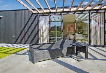 Sunny patio at Eco Lodge with modern black facade, wicker lounge chair, and large glass windows to living room.