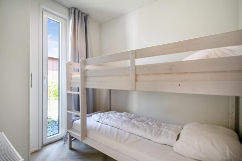 Dormitorio luminoso en Eco Lodge con literas blancas y ventana alta con cortinas neutras y luz natural.