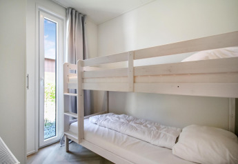 Dormitorio luminoso en Eco Lodge con literas blancas y ventana alta con cortinas neutras y luz natural.