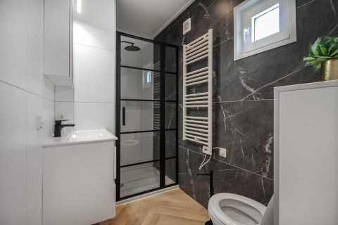 Baño moderno en Eco Lodge con cabina de ducha negra, lavabo elegante, inodoro y ventana luminosa.