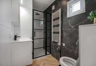 Baño moderno en Eco Lodge con cabina de ducha negra, lavabo elegante, inodoro y ventana luminosa.