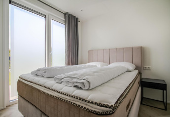 Bright and modern bedroom at Eco Lodge featuring a large bed, minimalist decor and big frosted windows.