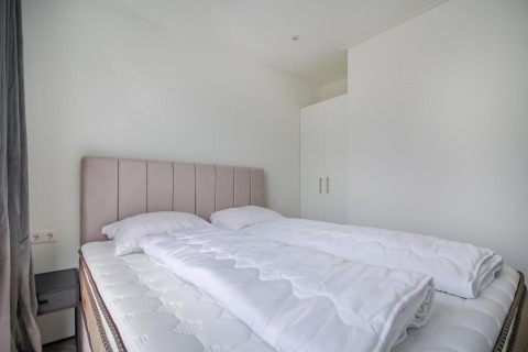 Moderne og minimalistisk soveværelse med dobbeltseng, hvide sengetøj og garderobeskab på Eco Lodge.