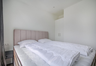 Dormitorio moderno y minimalista con cama doble, ropa de cama blanca y armario en Eco Lodge.
