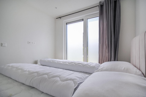 Dormitorio moderno de Eco Lodge con edredones blancos, grandes ventanales esmerilados y cortinas grises.