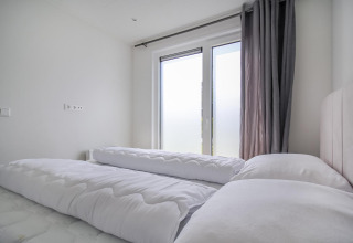 Lyst og moderne soveværelse på Eco Lodge med store vinduer, hvide dyner og grå gardiner.