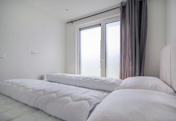 Dormitorio moderno de Eco Lodge con edredones blancos, grandes ventanales esmerilados y cortinas grises.