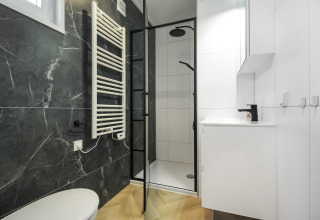 Baño moderno en blanco y negro en Eco Lodge, con ducha, radiador toallero y diseño elegante y minimalista.